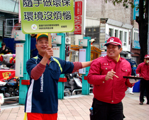 經由慈濟志工的解說後，民眾黃先生(左)自告奮勇地拿著標語舉牌，在一旁來來回回的走動，還不時提醒同行的人「這要回收」。(攝影者：曾于恩，地點：嘉義市文化公園、中正公園前，日期：2011/02/12)